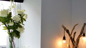 A living room with a window, a vase with flowers, a wooden sculpture, and a couch with patterned pillows.