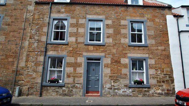 A stone building with three windows on the ground floor and two on the upper floor, each with shutters.
