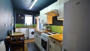 A compact kitchen with a washing machine, a stove, and cabinets. - One Shoregate- cosy Crail retreat (Crail)
