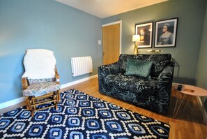 Ein Wohnzimmer mit Teppich und Sofa mit Muster, ein Holzstuhl und ein kleiner runder Tisch.