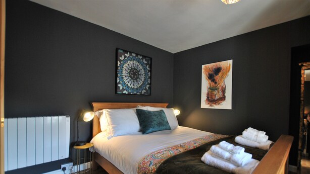 A bedroom with a bed, bedside lamps, a radiator, and artwork on the walls. - One Shoregate- cosy Crail retreat (Crail)