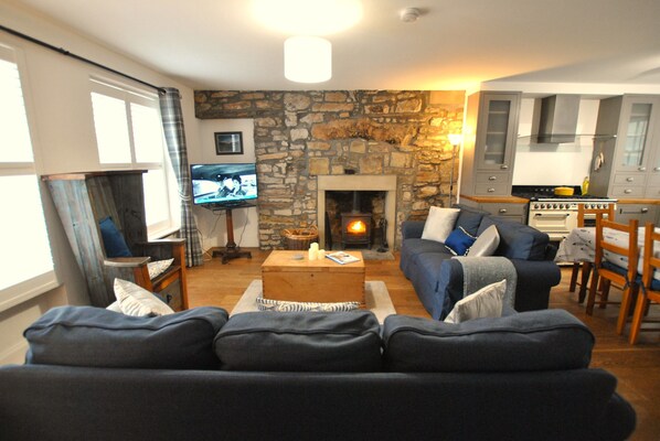 A cozy living room with a stone fireplace, a television, and a kitchen area.