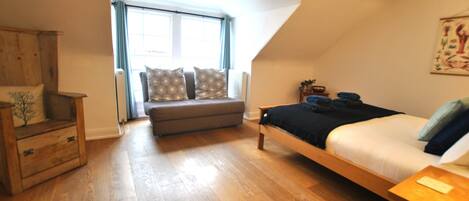 A bedroom with a loft bed, a wooden dresser, a bench, and a window with curtains.
