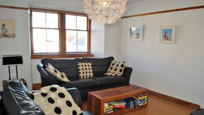 Ein Wohnzimmer mit einem schwarzen Ledersofa, einem Couchtisch mit Gesellschaftsspielen und einem großen Fenster mit Jalousien.