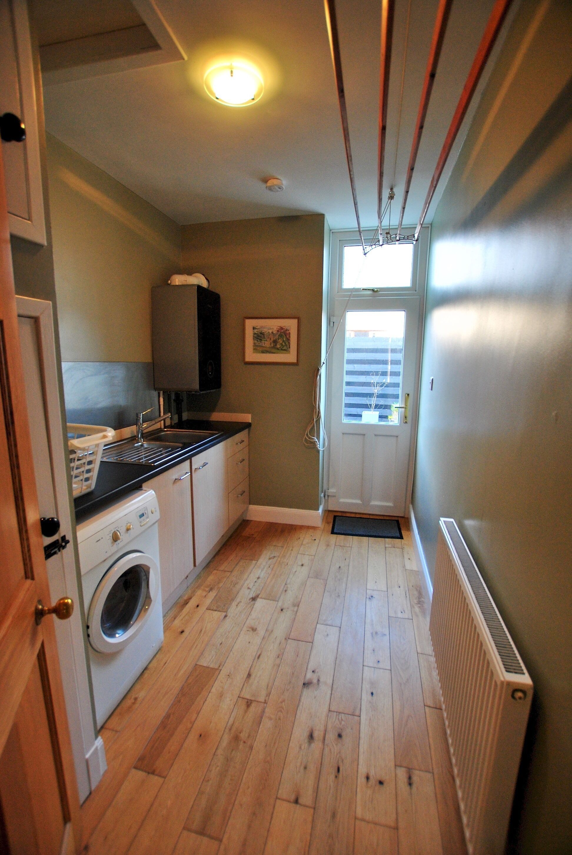 A narrow laundry room with a washing machine, a sink, and a drying rack.