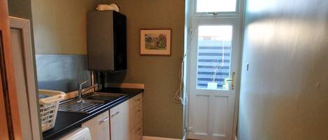 A narrow laundry room with a washing machine, a sink, and a drying rack.