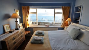 Un dormitorio con una cama grande, dos lámparas de noche, un aparador y vistas al mar a través de una ventana.