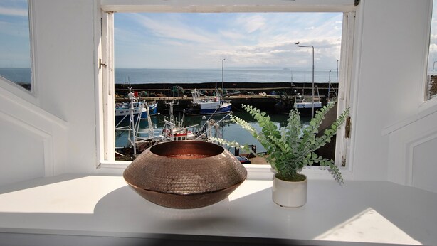 Vista da janela com interior branco, uma tigela de cobre pendurada e uma planta em vaso.