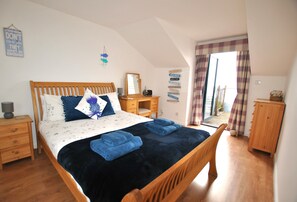 A bedroom with a wooden bed, a nightstand, a dresser, and a window with curtains.