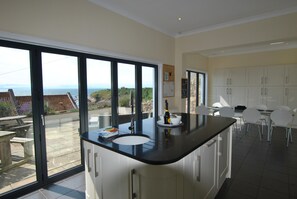 A modern kitchen with a large island, a dining area with white chairs, and a view of the sea through large windows. - Anchor House Pittenweem - Seaview home (Pittenweem)