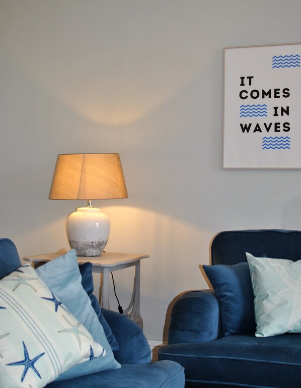 A room with a blue sofa, a white lamp on a small table, and a wall with a framed text.