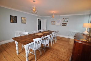 A dining room with a wooden table and white chairs, framed pictures on the wall, and a radiator.