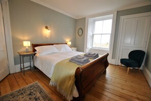 A bedroom with a wooden bed, bedside lamps, a window, and a chair.