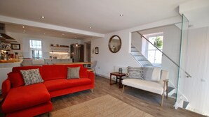 Een moderne woonkamer met een rode bank en een witte bank, met een keuken op de achtergrond en een glazen trap.