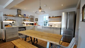 Een moderne keuken met een houten tafel en bank, roestvrijstalen apparatuur en witte kastjes.