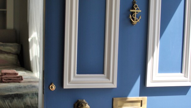 Una puerta azul con marcos de fotos blancos, un timbre de latón y un tirador de lat ón.