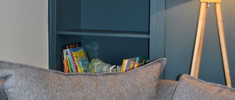 A grey sofa with patterned cushions, a bookshelf with books and decorative items, and a floor lamp.