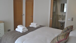 A hotel room with a bed, a grey blanket, two wooden doors, a bathroom with a sink, and a mirror. - Coastal Rest-  superb East Neuk townhouse (Anstruther)