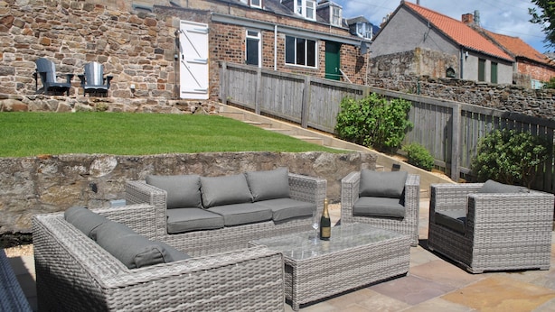 A stone house with a stone wall, a wooden deck, and outdoor furniture including a sofa and chairs. - Coastal Rest-  superb East Neuk townhouse (Anstruther)