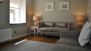 A living room with a sofa, two side tables, a lamp, and a window with blinds. - Coastal Rest-  superb East Neuk townhouse (Anstruther)