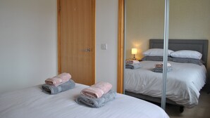 Ein Hotelzimmer mit zwei Betten, einer Holztür, einem Spiegel und einer Nachttischlampe.