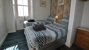 A bedroom with two beds, a dresser, a window, and a wooden wall panel. - Harbourside- home by the sea in coastal village (Saint Monans)