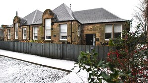 Een gebouw van steen met een grijs dak, een houten hek en sneeuw op de grond.