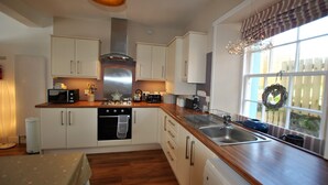 A kitchen with white cabinets, a stainless steel range hood, a wooden countertop, and a window with a view of the outside. - Turnstone- beautiful coastal home, Pittenweem (Pittenweem)