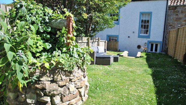 A stone wall, a blue building with windows, and a grassy yard with a bench. - Turnstone- beautiful coastal home, Pittenweem (Pittenweem)