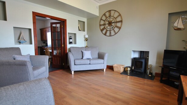 A living room with a grey sofa, a wooden floor, a fireplace, and a television. - The Beacon-  coastal home in St Monans (Saint Monans)