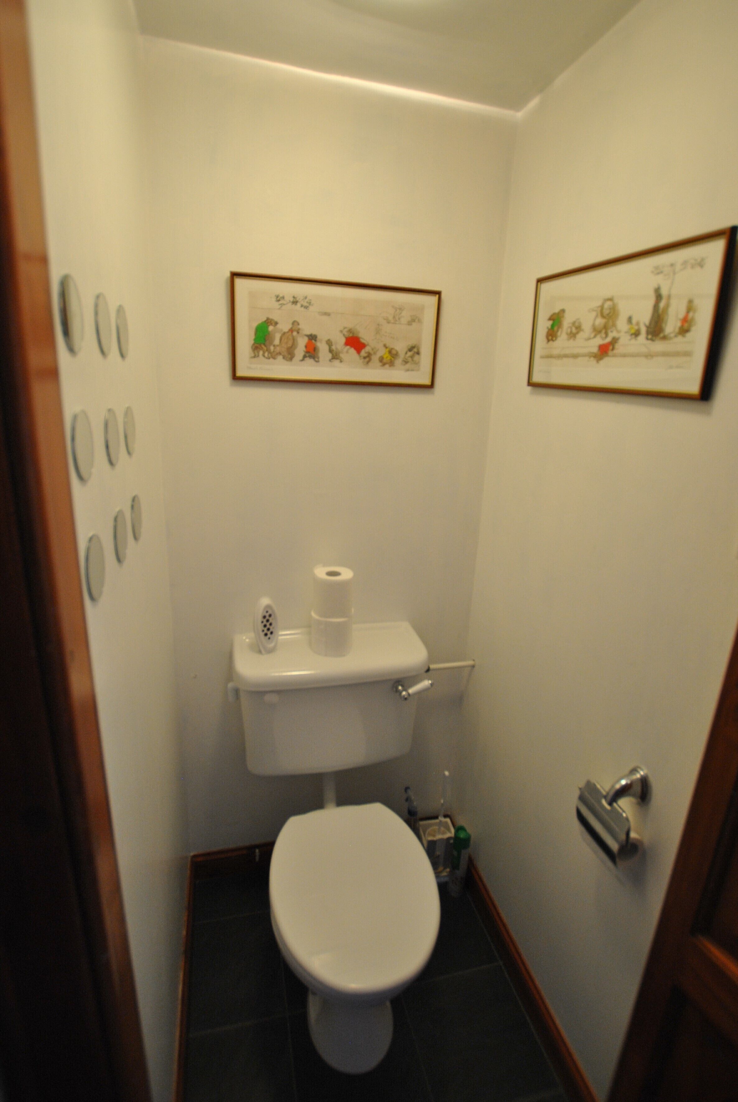 A small bathroom with a toilet, a roll of toilet paper, and two framed pictures on the wall.