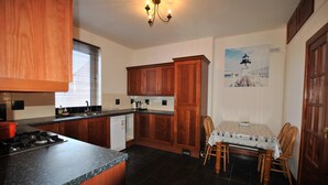 A kitchen with wooden cabinets, a gas stove, a sink, and a dining table with chairs. - The Beacon-  coastal home in St Monans (Saint Monans)