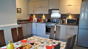 A modern kitchen with a dining table set for breakfast, including croissants and fruit.