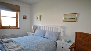 Een slaapkamer met een bed, nachtkastjes, een stoel en een raam met gordijnen.