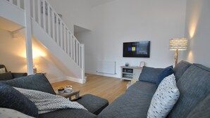 A modern living room with a grey sofa, a small side table, a remote control, and a television on the wall.