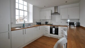 A modern kitchen with white cabinets, a wooden countertop, a built-in oven, and a window providing natural light.