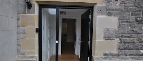 A stone building entrance with a wooden door, a doormat, and a black lantern.