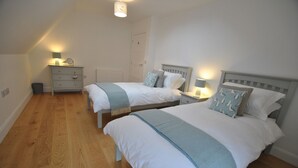 A bedroom with two single beds, a bedside table with a lamp, a dresser, and a waste bin.