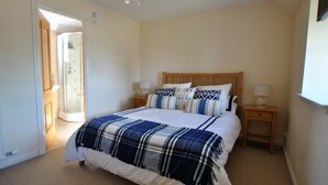 A bedroom with a bed, bedside tables, a nightstand, a wooden headboard, and a door leading to a bathroom. - Seaview Steading-spacious home in rural location (Crail)