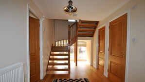 A hallway with wooden flooring, a black and white patterned rug, a wooden staircase, and wooden doors. - Seaview Steading-spacious home in rural location (Crail)