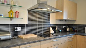A modern kitchen with a black and white tiled backsplash, wooden cabinets, and a stainless steel range hood. - Seaview Steading-spacious home in rural location (Crail)