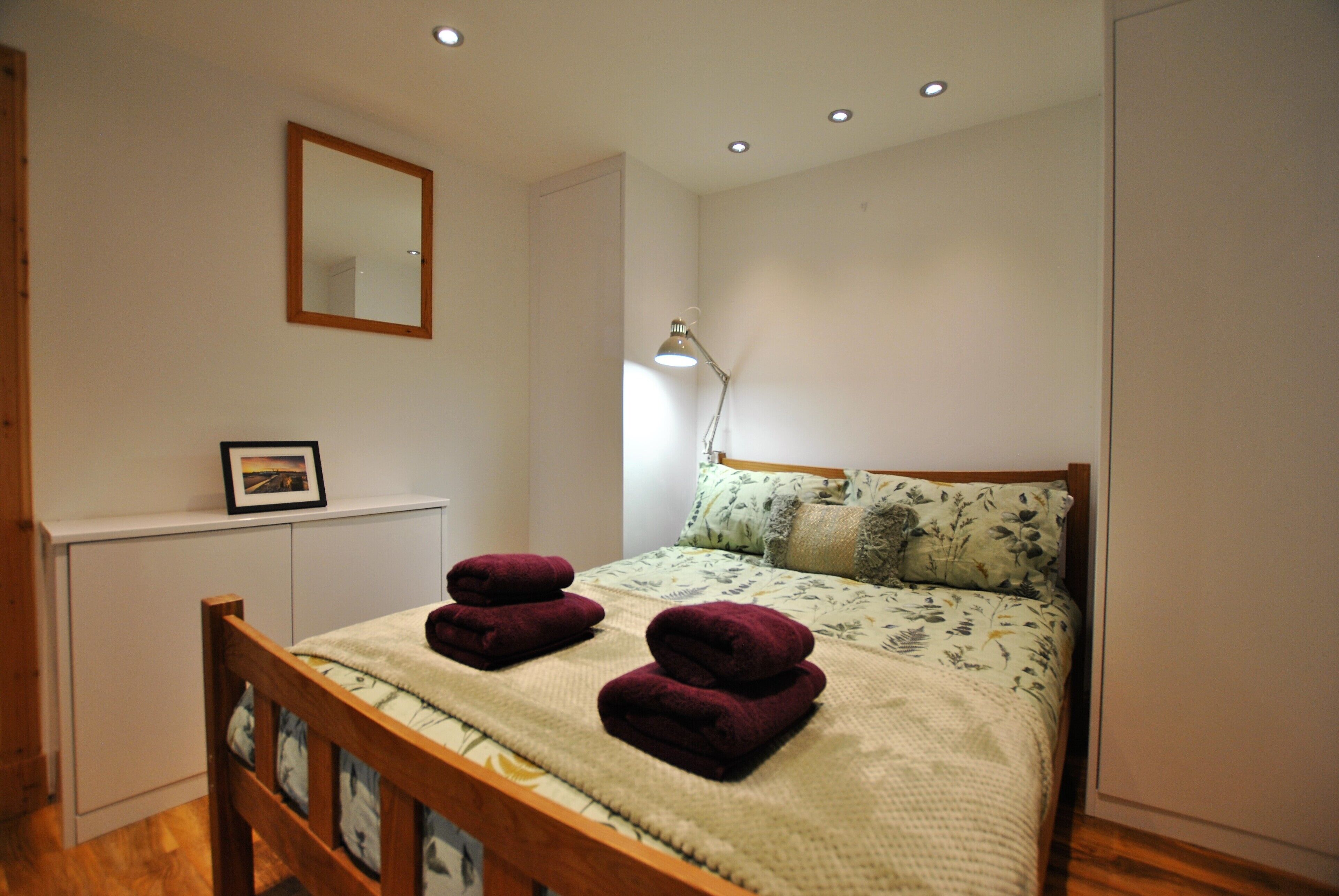 A bedroom with a bed, a bedside table, a lamp, a mirror, and a picture frame.