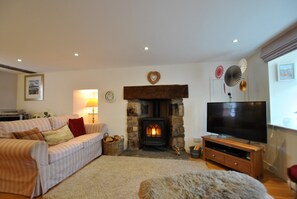 A cozy living room with a stone fireplace, a television on a wooden stand, and a striped sofa.