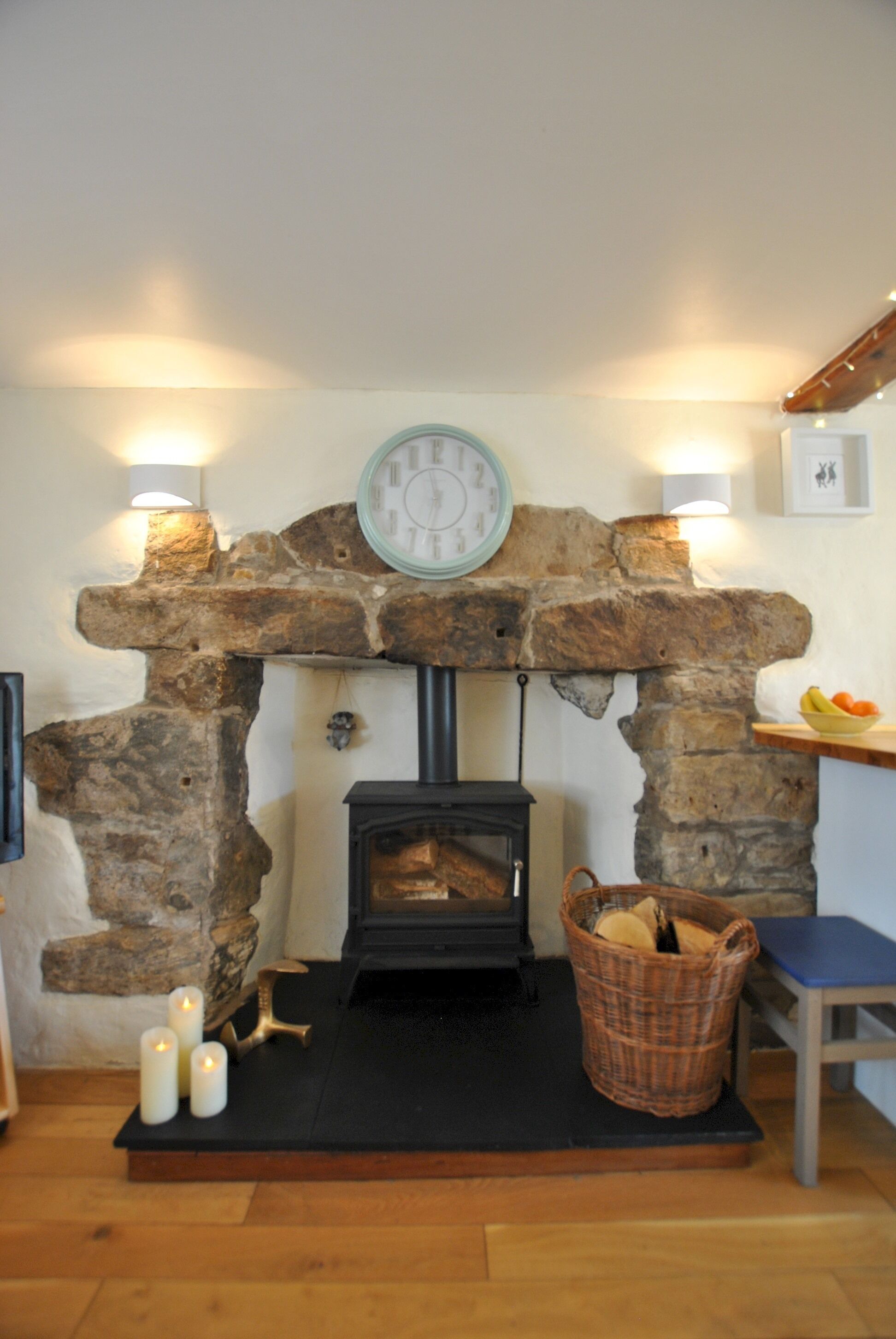 Una habitación acogedora con chimenea de piedra, un reloj y una cesta de leña.