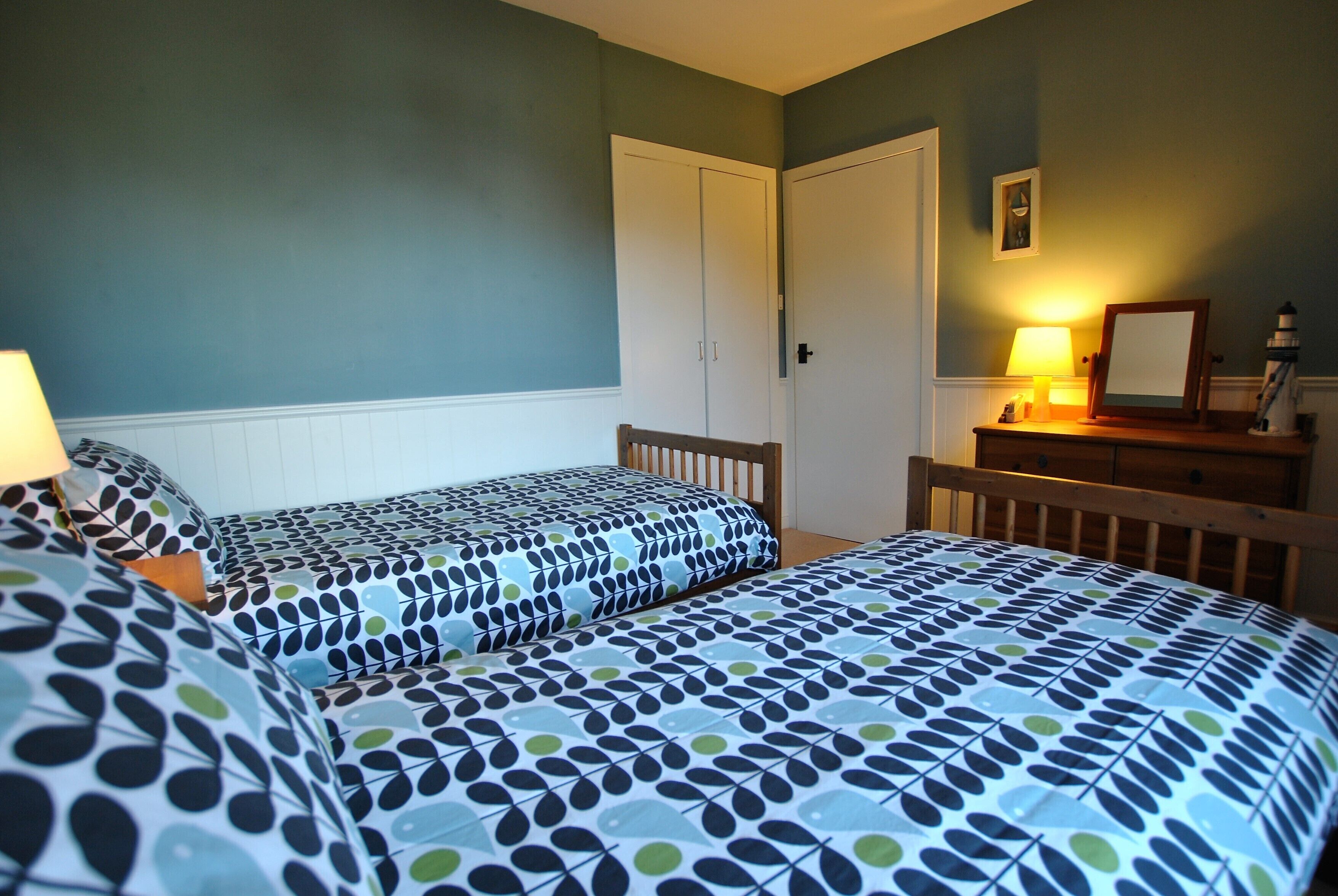 A bedroom with two beds, a dresser, a lamp, and a framed picture on the wall.