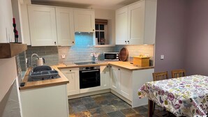 A compact kitchen with white cabinets, a microwave, a kettle, and a wooden countertop. - Willow Cottage- charming cottage in East Neuk (Pittenweem)