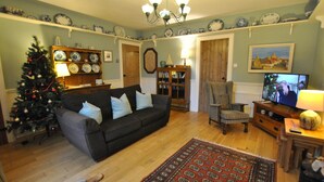 A living room with a dark-colored sofa, a Christmas tree, a wooden coffee table, a patterned rug, and a television. - Willow Cottage- charming cottage in East Neuk (Pittenweem)