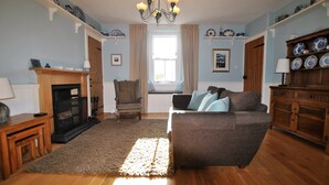 A living room with a fireplace, a sofa, a chair, and a wooden cabinet. - Willow Cottage- charming cottage in East Neuk (Pittenweem)