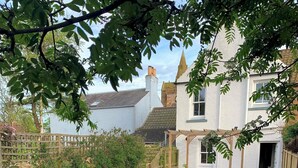 A garden with a patio area featuring a white sofa set, a wooden pergola, and a stone pathway. - Willow Cottage- charming cottage in East Neuk (Pittenweem)