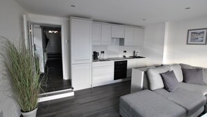 Et moderne køkken med hvide skabe, en grå sofa og en potteplante.